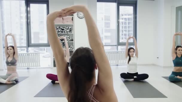 Die junge Yogalehrerin zeigt Gleichgewichtspositionen und spricht mit Studenten, während andere Frauen schweigend Haltungen wiederholen. Gruppenpraxiskonzept. — Stockvideo
