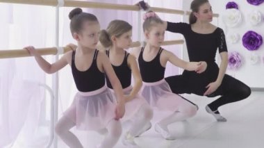 Yoğunlaşmış kızlar dans okulunda temel bale pozisyonlarını öğreniyorlar. Dikkatli bir öğretmen zor duruşlarda ustalaşmalarına yardımcı oluyor..