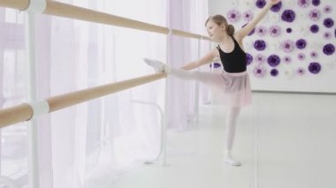 Dans stüdyosunda bacak esnetme egzersizleri yaparken küçük kızlar bale çubuğu kullanıyor.