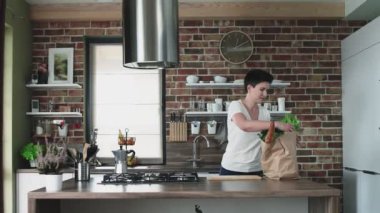 Mutlu genç bayan mutfağa büyük bir kese dolusu yiyecek getiriyor..