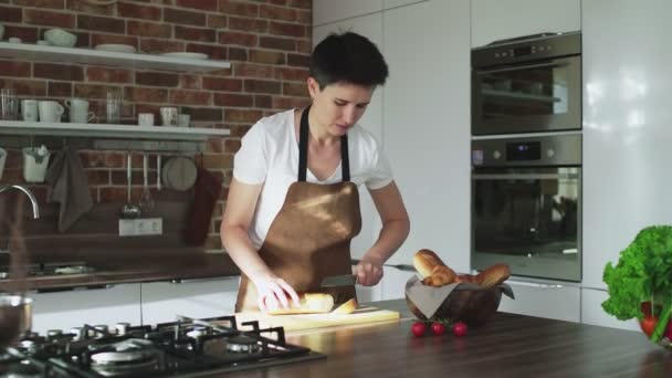 Kvinna förbereder frukost, skära baguette på en bräda i köket — Stockvideo