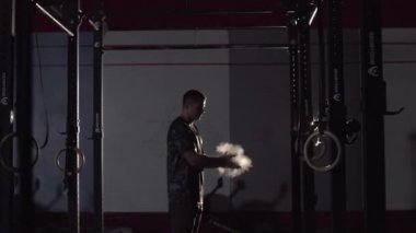 Spor giyimli genç adam spor salonunda magnezya ile antrenman yapmaya ve el çırpmaya hazırlanıyor..