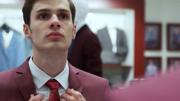 Muž se dívá do zrcadla a nosí červenou bundu v butiku. — Stock video
