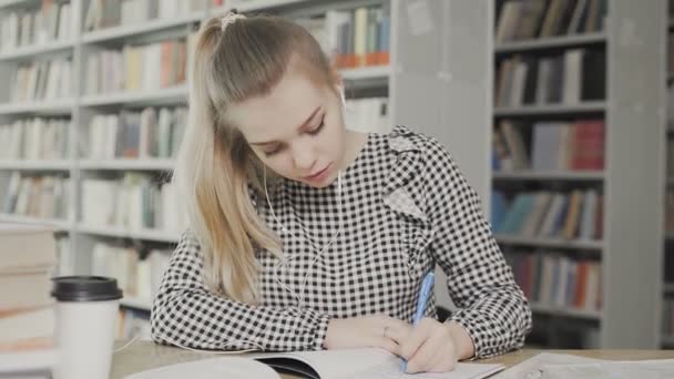 Jovem estudante escrevendo em seus livros didáticos na biblioteca — Vídeo de Stock