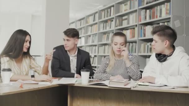 Jóvenes estudiantes charlan en la biblioteca universitaria . — Vídeos de Stock