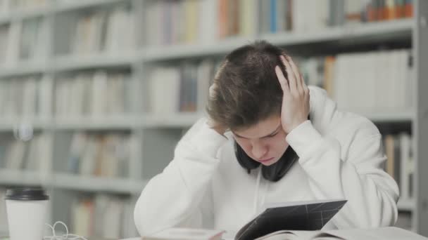 Trøtt student forbereder seg til eksamen på universitetsbiblioteket – stockvideo