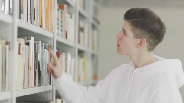 Homem à procura de livro em estantes na biblioteca na faculdade — Vídeo de Stock