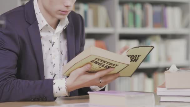 Dolly záběr mladého studenta pilně studovat v knihovně. Muž univerzitní student dělá výzkum v knihovně s knihami — Stock video