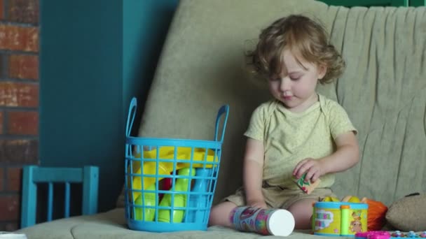 Маленька дівчинка грає зі своїми іграшками на дивані . — стокове відео