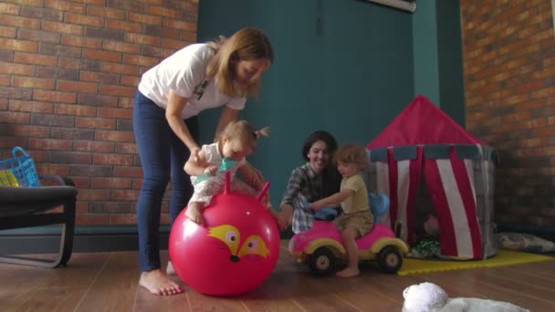Las mamás con niños jugando. Chica saltando en una bola roja — Vídeo de stock
