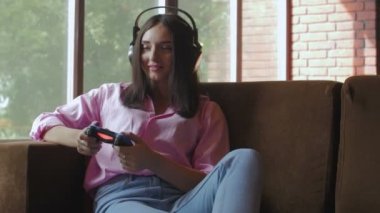 Kulaklıklı genç bir kadın oyun oynarken joystick kullanıyor.