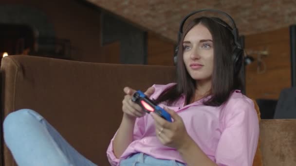 Vrouw met hoofdtelefoon zit op de bank en het spelen van video game — Stockvideo