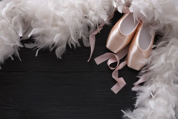 Pink ballet pointe shoes and feather on black wood background