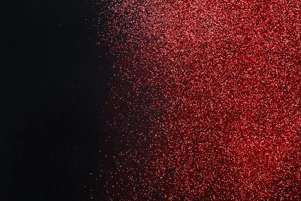 Red glitter sand texture on black, abstract background.