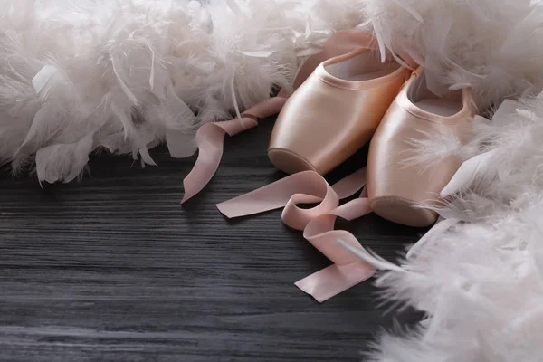 Pink ballet pointe shoes and feather on black wood background