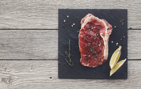 暗い木製のテーブル背景、上面に生の牛肉ステーキ — ストック写真