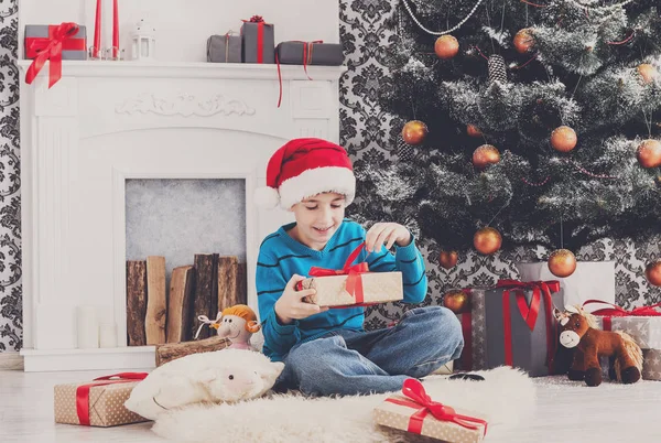 Ładny chłopak w santa hat rozpakowaniu prezentów — Zdjęcie stockowe