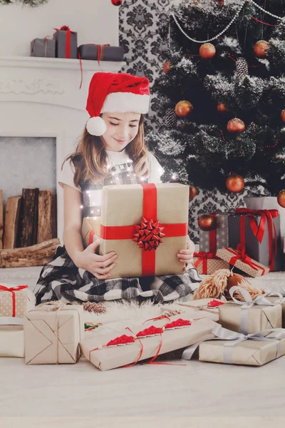 Menina bonita em santa chapéu desembrulhando presentes de Natal — Fotografia de Stock