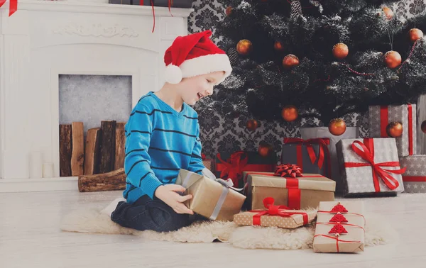 Lindo chico en santa sombrero desenvolver regalos de Navidad —  Fotos de Stock