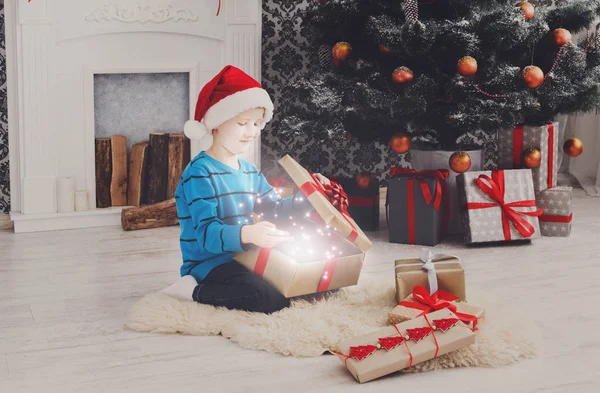 Bonito menino feliz em santa chapéu desembrulhando presentes de Natal — Fotografia de Stock