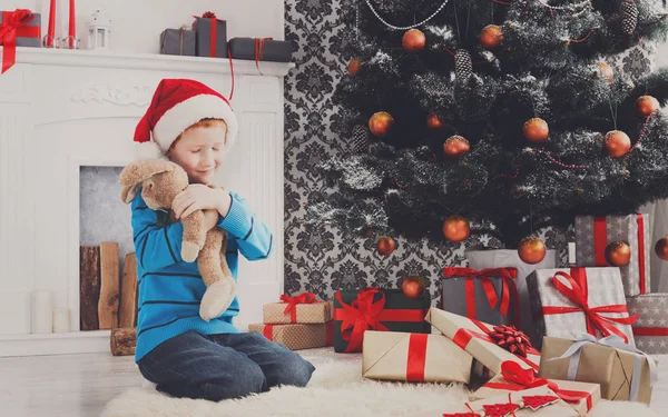 Süßer glücklicher Junge mit Weihnachtsmütze und Spielzeug-Weihnachtsgeschenken — Stockfoto