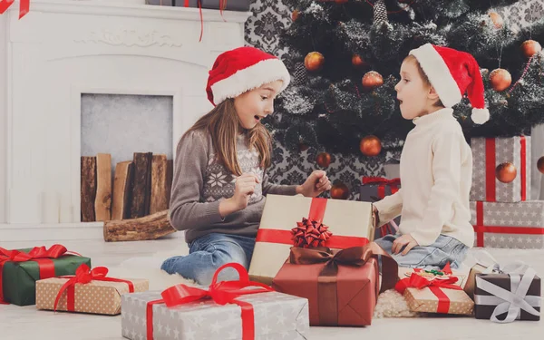 Enfants heureux dans chapeaux de Père Noël déballer cadeaux de Noël — Photo