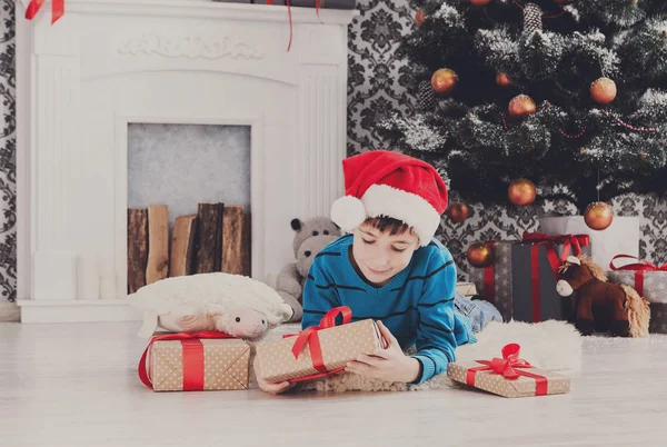 Menino bonito em santa chapéu desembrulhando presentes de Natal — Fotografia de Stock