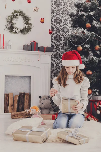 Piękna dziewczyna w santa hat rozpakowaniu prezentów — Zdjęcie stockowe