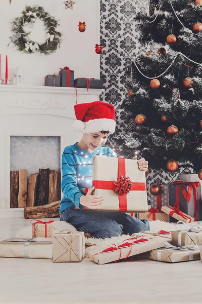 Bonito menino feliz em santa chapéu desembrulhando presentes de Natal — Fotografia de Stock