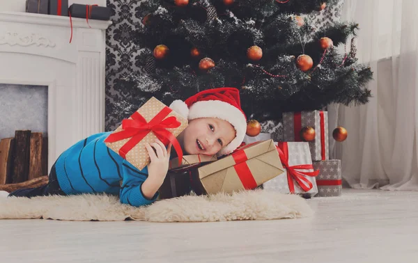 Menino bonito em santa chapéu desembrulhando presentes de Natal — Fotografia de Stock