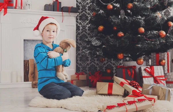 Süßer glücklicher Junge mit Weihnachtsmütze und Spielzeug-Weihnachtsgeschenken — Stockfoto