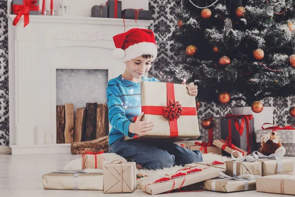 Bonito menino feliz em santa chapéu desembrulhando presentes de Natal — Fotografia de Stock