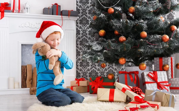 Süßer glücklicher Junge mit Weihnachtsmütze und Spielzeug-Weihnachtsgeschenken — Stockfoto