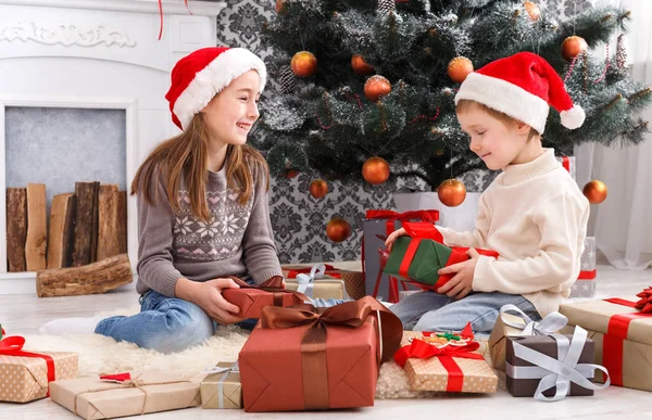 Niños felices en sombreros de Papá Noel desenvolviendo regalos de Navidad —  Fotos de Stock