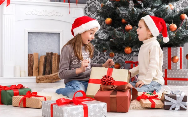 Enfants heureux dans chapeaux de Père Noël déballer cadeaux de Noël — Photo