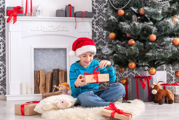 Menino bonito em santa chapéu desembrulhando presentes de Natal — Fotografia de Stock