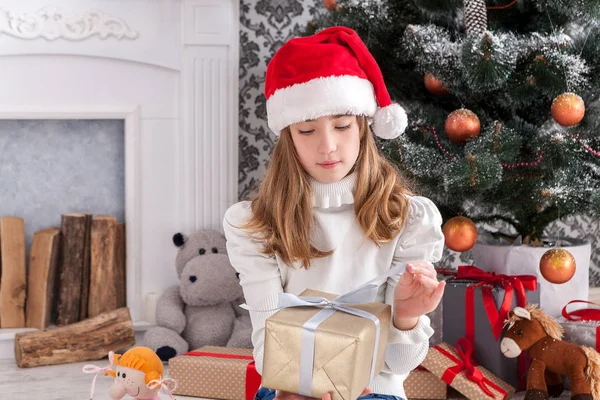 Schönes Mädchen mit Weihnachtsmütze beim Auspacken von Weihnachtsgeschenken — Stockfoto