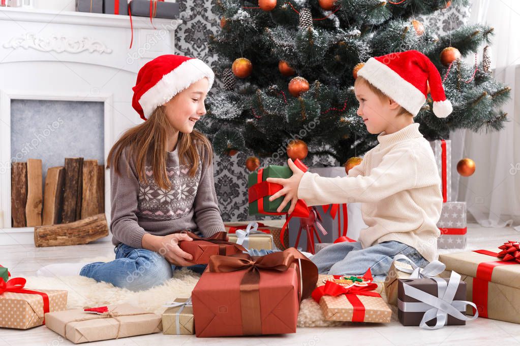 Happy children in santa hats unwrapping christmas presents