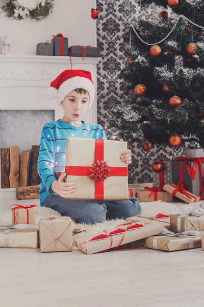 Bonito menino feliz em santa chapéu desembrulhando presentes de Natal — Fotografia de Stock