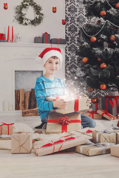 Bonito menino feliz em santa chapéu desembrulhando presentes de Natal — Fotografia de Stock