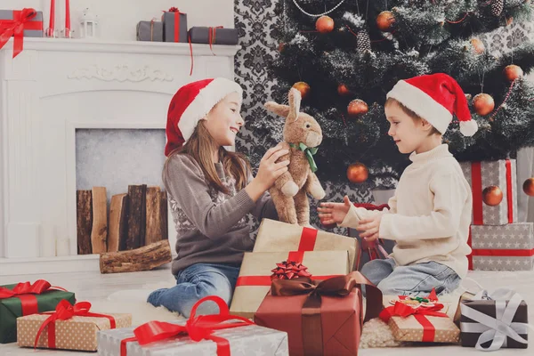 Niños felices en sombreros de Papá Noel desenvolviendo regalos de Navidad —  Fotos de Stock