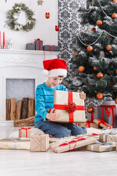 Menino bonito em santa chapéu desembrulhando presentes de Natal — Fotografia de Stock