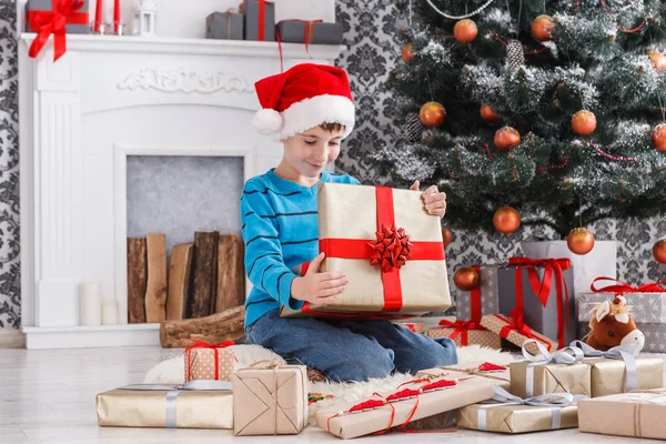 Menino bonito em santa chapéu desembrulhando presentes de Natal — Fotografia de Stock