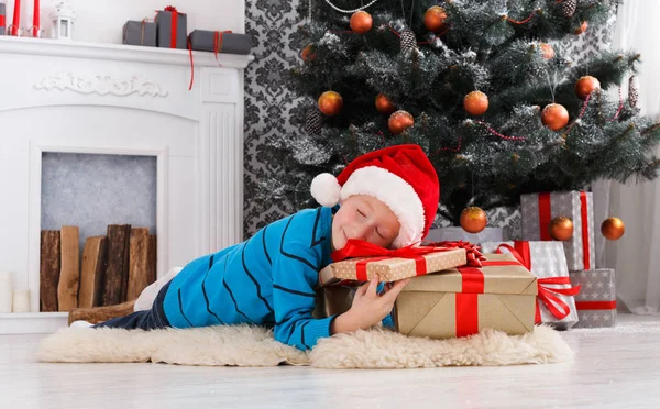 Menino bonito em santa chapéu desembrulhando presentes de Natal — Fotografia de Stock