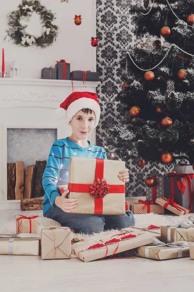 Ładny chłopak szczęśliwy w santa hat rozpakowaniu prezentów — Zdjęcie stockowe
