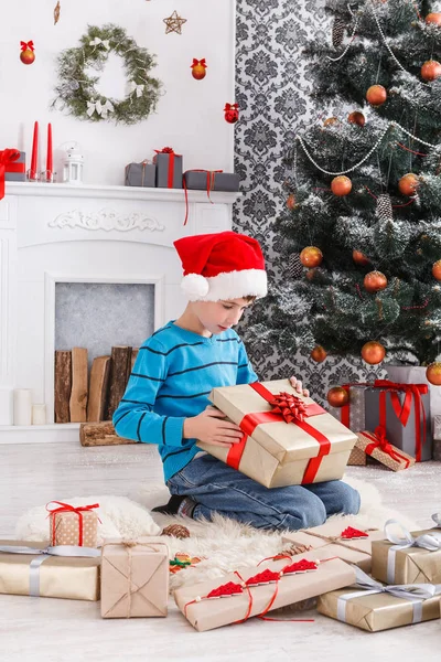 Süßer Junge mit Weihnachtsmütze beim Auspacken von Weihnachtsgeschenken — Stockfoto