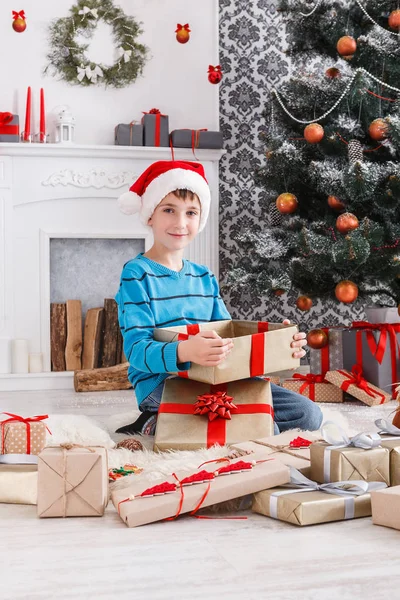 Ładny chłopak w santa hat rozpakowaniu prezentów — Zdjęcie stockowe