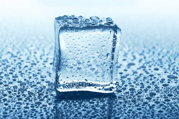 Transparenter Eiswürfel mit Reflexion auf blauem Glas mit Wassertropfen — Stockfoto