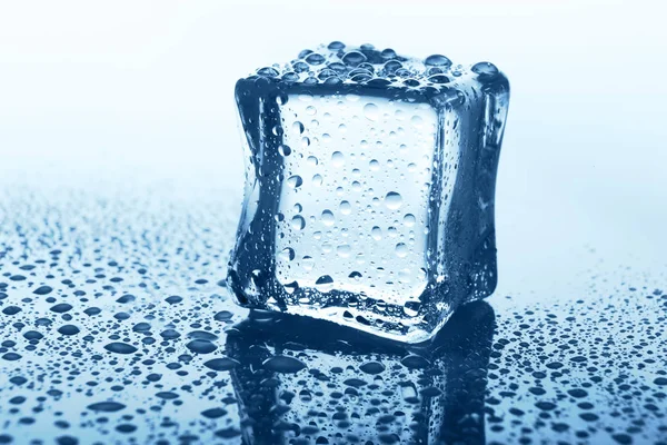 Cubo de gelo transparente com reflexão em vidro azul com gotas de água — Fotografia de Stock