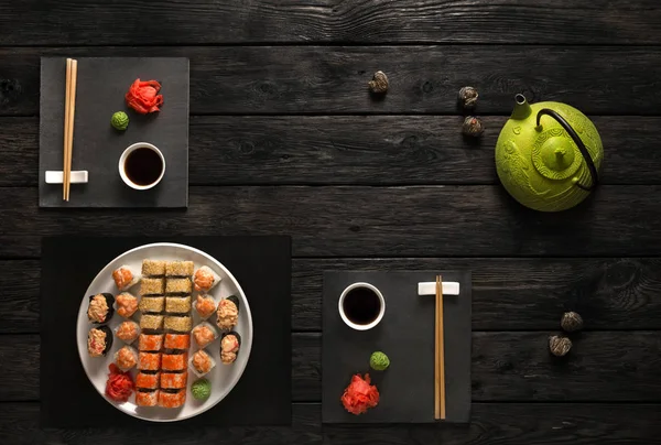 Set de sushi y rollos con tetera en madera rústica negra, vista superior — Foto de Stock